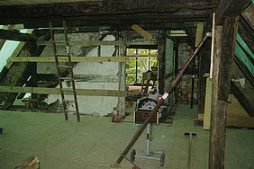 mit neuen Brettern gesicherte, bauzeitliche Wandscheibe (ausgefüllte Fachwerkwand) in einem Dachraum, daneben Baustellenleitern und Werkzeug