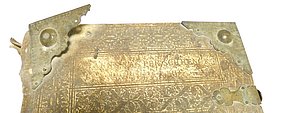Oben auf dem Einband der Bibel steht der Name des Buchs. Er ist lateinisch. Die Ecken des Einbandes haben Metallkappen. Sie sind verziert. An der Seite hat das Buch einen Verschluss.