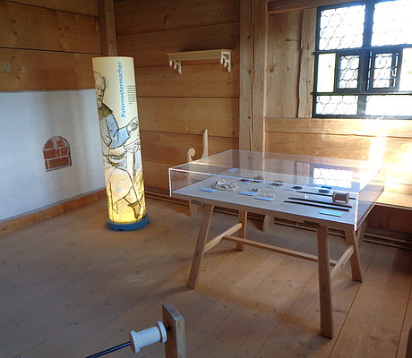 FFM_Badhaus_Wendelstein_Paternosterer_als_Mieter ein Tisch mit Exponaten, durch Glas geschützt sowie ein stehender Zylinder mit Ausstellungstext