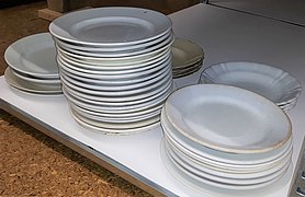 In einem Regal liegen viele weiße Teller. Die Teller sind gestapelt.