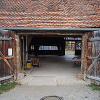 FFM_Hinterer_Eingang_Alter_Bauhof Fotoaufnahme des hinteren Eingangs vom Alten Bauhof aus Bad Windsheim. Das zweiflügelige Holztor ist nach außen geöffnet. An der rechten Seite hängt ein „Rauchen verboten“-Schild. Das Dach nimmt das obere Drittel des Bildes ein und ist mit Sechseck-Flachziegeln gedeckt.