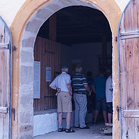 FFM_West_Kommunbrauhaus_Eingang Fotoaufnahme des Eingangsbereichs vom Kommunbrauhaus aus Schlüsselfeld am aktuellen Standort. Die zweiflüglige Holztür ist nach außen geöffnet, im Inneren befindet sich eine Besuchergruppe. Der Boden vor dem Gebäude ist gepflastert.