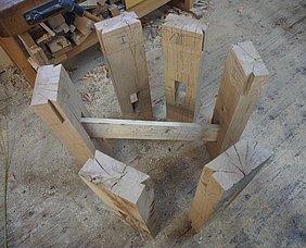 Die sechs Kopfhölzer sind entsprechend ihrer Lage am Mühlrad in einem kleinen Kreis von etwa 50 cm Durchmesser aufgestellt. Jeweils die beiden Kopfhölzer, die sich an den beiden Enden einer Speiche gegenübersitzen, stehen einander gegenüber. Die Verzapfung zwischen Speiche und Kopfholz wird auf jedem der drei Fotos mit einem Brett von ca. 50 cm Länge simuliert. Die Position der Verzapfung ist an vier Kopfhölzern seitlich versetzt. Eine Speiche sitzt genau mittig.