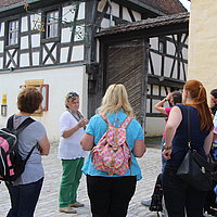 Fotoaufnahme einer allgemeinen Überblicksführung für Erwachsene. Die Gruppe Frauen steht auf dem gepflasterten Hof vor dem Wirtshaus am Kommunbrauhaus. Sie blicken zu dem Fachwerkhaus empor. An der Fassade hängt ein Brauerstern mit Maßkrug in der Mitte.