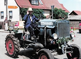 Der Schlepper ist hellblau. Auf ihm sitzt sein Erbauer.