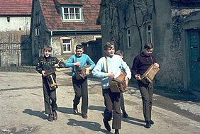 Vier Jungen laufen auf der Straße. Sie tragen Ratschen. Sie klappern und machen Krach.