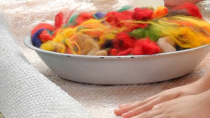eine Schüssel mit bunter Filzwolle, daneben filzende Hände