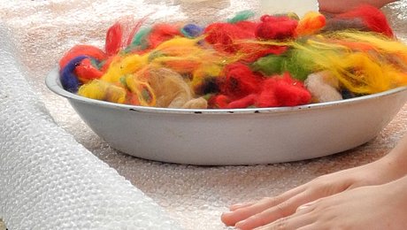 eine Schüssel mit bunter Filzwolle, daneben filzende Hände