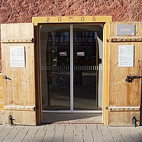 FFM_Eingangsbereich_Kasse Fotoaufnahm der geöffneten Eingangstür zur Museumskasse im Korbhaus aus Knittelsbach am aktuellen Standort. In den Türrahmen wurden die Jahreszahl „2006“, sowie das Fränkische Wappen eingeprägt. Hinter der Holztür befindet sich eine automatische Schiebetür.