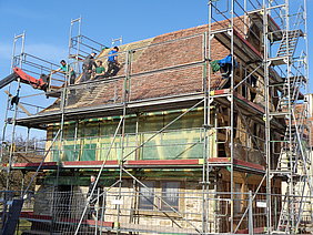 Eingerüstete Synagog aus Allersheim mit Dachdeckern am Werk