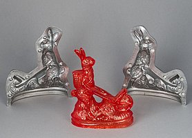 Auf dem Bild ist eine Gussform. Sie ist aus Aluminium. Sie ist aus zwei Hälften. Mit ihr kann man einen Zuckerhasen gießen. Der Zuckerhase ist rot. Er hat eine Schubkarre.