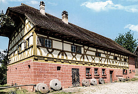 Ein- bzw. zweistöckiger Bau der Mühle aus Unterschlauersbach im Fränkischen Freilandmuseum Bad Windsheim; Bau mit massivem Erdgeschoss und Fachwerkobergeschoss, Satteldach mit weitvorkragendem Halbwalm am Südgiebel, Biberschwanz-Doppeldeckung