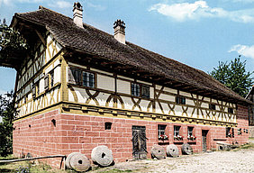 Ein- bzw. zweistöckiger Bau der Mühle aus Unterschlauersbach im Fränkischen Freilandmuseum Bad Windsheim; Bau mit massivem Erdgeschoss und Fachwerkobergeschoss, Satteldach mit weitvorkragendem Halbwalm am Südgiebel, Biberschwanz-Doppeldeckung