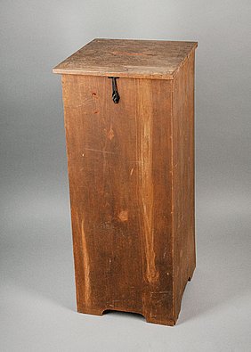 Die Wahlurne ist ein Kasten aus Holz. Im Deckel ist ein Schlitz. Der Kasten kann verschlossen werden.