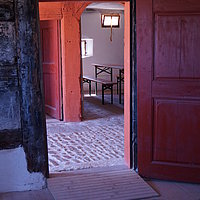 FFM_Unterlindelbach_Rampe_Stube Fotoaufnahme der Tür zur Stube im Bauernhaus aus Unterlindelbach am aktuellen Standort. Vor der Schwelle der Holztür liegt eine Rampe. Im Raum dahinter steht eine Bierzeltgarnitur.