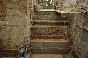 Treppe zur Badstube Fotoaufnahme der rekonstruierten Treppe zur Badstube. Die Stufen bestehen aus Sandstein und wurden teilweise mit Ziegelsteinen untermauert. Links befindet sich ein Mauerwerk aus Sandsteinquadern und Ziegeln. Davor steht eine Kabeltrommel, deren Kabel über die Treppe führt.