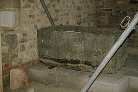 Muschelkalkbecken Fotoaufnahme eines Muschelkalkbeckens aus dem Museumsfundus. Das teilweise mit Moos bewachsene Becken befindet sich auf einer Steinplatte, es wurden Holzstücke untergelegt. Im Hintergrund ist ein Bruchsteinmauerwerk erkennbar.