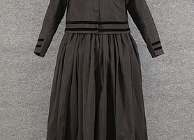 Das Bild ist schwarzweiß. Die Frau hat ein langes Gewand an. Das Gewand ist dunkel.