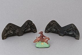 Die Gussform ist aus Eisen. In ihr wurde eine Figur aus Blei gegossen. Die Figur ist ein laufender Hase. Auf ihm reitet ein kleinerer Hase. Die Figur hat man ins Schaufenster gestellt.