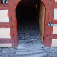 FFM_Unterlindelbach_Haupteingang Fotoaufnahme des Haupteingangs vom Bauernhaus aus Unterlindelbach am aktuellen Standort. Vor der Schwelle der geöffneten Holztür liegt eine Rampe. An der Hauswand rechts im Bild wurde ein Geländer aus Holz angebracht.
