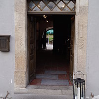 FFM_Gasthaus_zur_Krone_Haupteingang Fotoaufnahme des Haupteingangs vom Gasthaus zur Krone am aktuellen Standort. Zur nach innen geöffneten Holztür führt eine Steinstufe, darauf steht rechts eine Laterne mit Kerze. Davor liegt ein Fußabstreifer. Über der Tür hängt eine Lampe, links daneben ein Briefkasten.