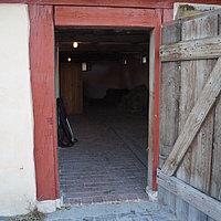 FFM_Unterlindelbach_Eingang_Kuhstall Fotoaufnahme des Eingangs zum Kuhstall aus Unterlindelbach am aktuellen Standort. Die Holztür ist nach außen geöffnet. Der Boden im Inneren ist gepflastert, das Dach mit Sechseck-Flachziegeln gedeckt.