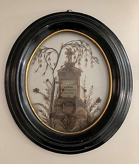 Das Bild ist oval. Der Rahmen ist aus Holz. Das Bild zeigt ein Denkmal. Es besteht aus Zweigen und Haaren.