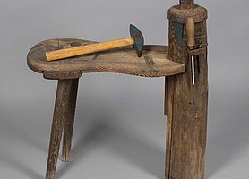 Der Dengelbock ist eine kleine Bank. Sie hat hinten zwei Beine. Vorne hat sie eine dicke Säule aus Holz. Auf der Säule ist ein Metallwürfel, der Amboss. An der Seite sind Werkzeuge befestigt. Die Werkzeuge sind ein Hammer, eine Feile und ein Schlüssel.
