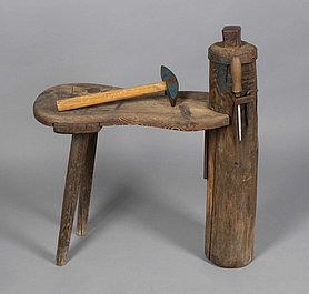 Der Dengelbock ist eine kleine Bank. Sie hat hinten zwei Beine. Vorne hat sie eine dicke Säule aus Holz. Auf der Säule ist ein Metallwürfel, der Amboss. An der Seite sind Werkzeuge befestigt. Die Werkzeuge sind ein Hammer, eine Feile und ein Schlüssel.