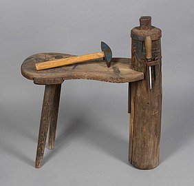 Der Dengelbock ist eine kleine Bank. Sie hat hinten zwei Beine. Vorne hat sie eine dicke Säule aus Holz. Auf der Säule ist ein Metallwürfel, der Amboss. An der Seite sind Werkzeuge befestigt. Die Werkzeuge sind ein Hammer, eine Feile und ein Schlüssel.