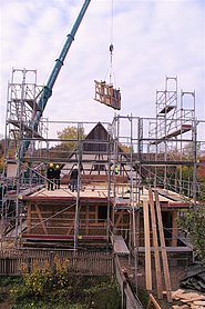Hausbaustelle mit Autorkran und daran schwebendem Wandteil