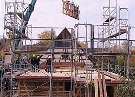 Hausbaustelle mit Autorkran und daran schwebendem Wandteil