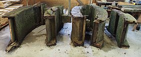 1)	Das kaputte Mühlrad wurde beim Abbau in vier gleichgroße Segmente zerlegt. Sie lagern in der Abbundhalle des Bauhofs.