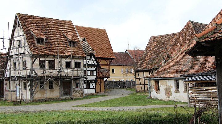 FFM_Stadt_Mittelaltergasse Fotoaufnahme der Gasse mittelalterlicher Fachwerkhäuser in der Baugruppe Stadt. An einem Weg befinden sich auf beiden Seiten verschiedene Fachwerkhäuser. Vorne links steht zum Beispiel das Handwerkerhaus aus Bad Windsheim, das von einem Holzgerüst umgeben ist.