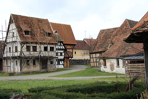 FFM_Stadt_Mittelaltergasse Fotoaufnahme der Gasse mittelalterlicher Fachwerkhäuser in der Baugruppe Stadt. An einem Weg befinden sich auf beiden Seiten verschiedene Fachwerkhäuser. Vorne links steht zum Beispiel das Handwerkerhaus aus Bad Windsheim, das von einem Holzgerüst umgeben ist.