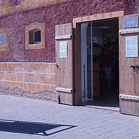 FFM_Knittelsbach_Kasse_Haupteingang Fotoaufnahme des Eingangsbereiches der Kasse, die sich im Korbhaus aus Knittelsbach befindet. In den Rahmen der geöffneten Holztür wurden die Jahreszahl „2006“, sowie das Fränkische Wappen eingeprägt. An der Tür hängen mehrere Schilder.