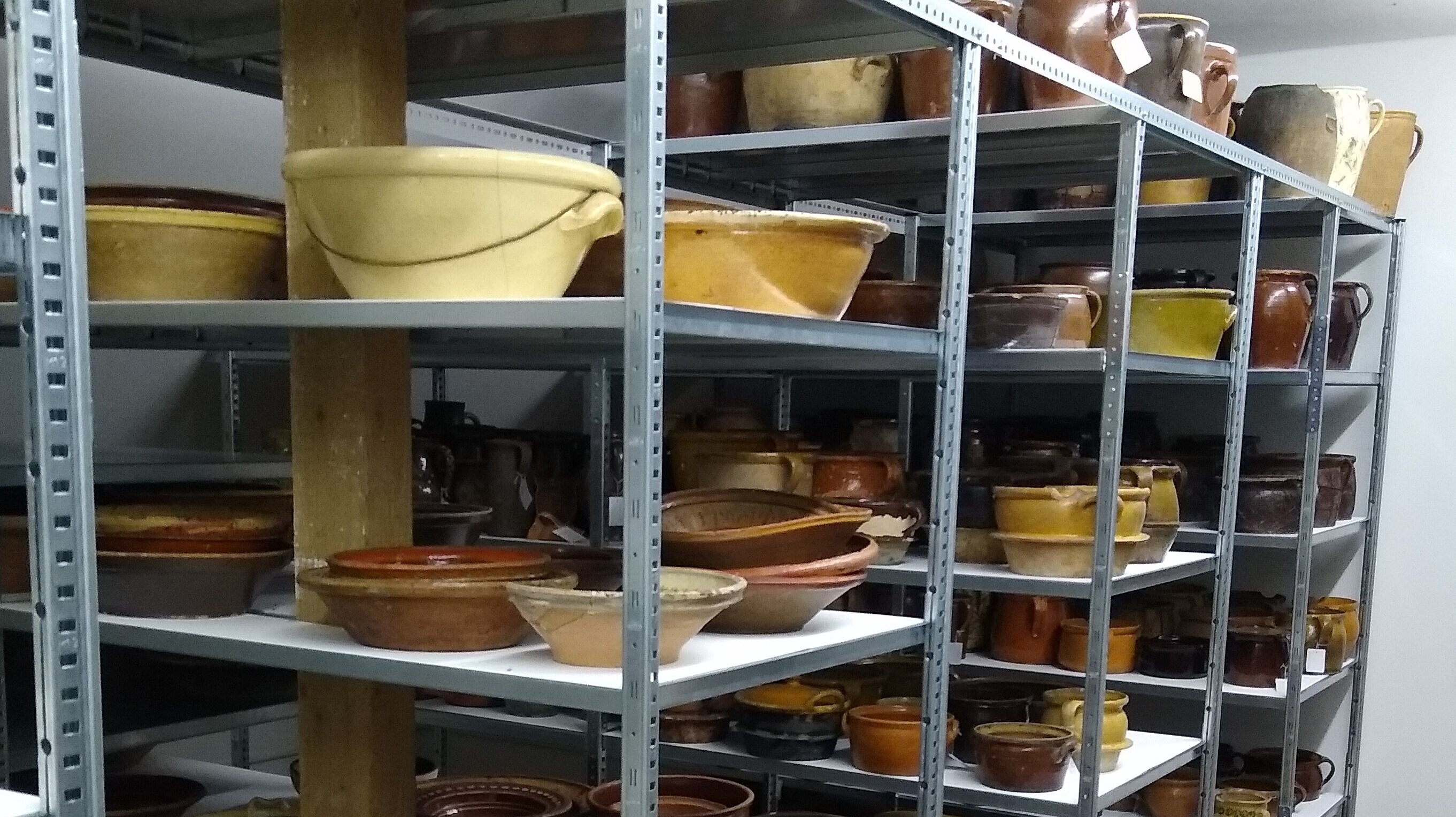 In den Regalen stehen Schüsseln und Töpfe. Sie sind aus Keramik.