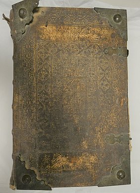 Die Bibel ist ein großes Buch. Der Einband ist aus Leder. Das Leder ist verziert. Die Ecken des Einbandes haben Metallkappen. Die Kappen schützen den Einband.