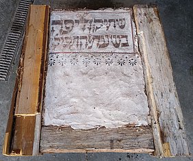Das Gefach ist von Holzbalken gerahmt. Die Inschrift ist im oberen Bereich.