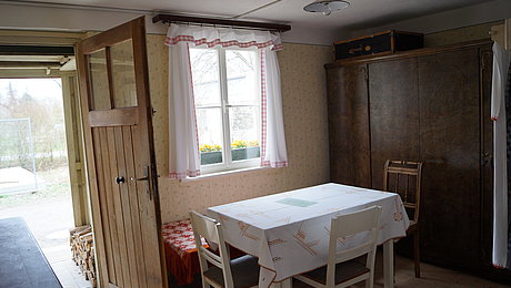 Die Stube des Behelfsheimes mit Tisch, Stühlen und großem Kleiderschrank