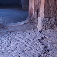 FFM_Mittelalter_Hoefstetten_Schwelle Fotoaufnahme der erhöhten Schwelle aus Holz, die zur Küche des Bauernhauses aus Höfstetten am aktuellen Standort führt. Der Boden der Küche besteht aus Holzdielen, der des vorderen Raumes aus gestampftem Lehm. Das Haus gehört zum mittelalterlichen Bauernhof.