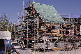 Das auf allen Seiten eingerüstete Badhaus aus Wendelstein, ein Drittel des Dachwerks ist schon aufgestellt und mit einer Plastikplane bedeckt.