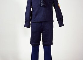 Der Anzug ist blau. Das Hemd ist blau und hat weiße Streifen am Kragen. Die blaue Hose ist kurz.