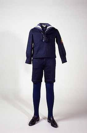 Der Anzug ist blau. Das Hemd ist blau und hat weiße Streifen am Kragen. Die blaue Hose ist kurz.