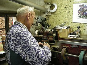 Der Schuster arbeitet an einer Maschine. Es ist eine Poliermaschine.