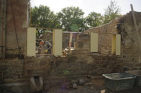 Fotoaufnahme der Nordfassade mit zwei Fensteröffnungen. Das fehlende Mauerwerk wird um die zukünftigen Fensteröffnungen rekonstruierend aufgemauert. Neben den Fensteröffnungen befinden sich Kästen, die die Position der später einzusetzenden Sandsteingewände markieren. 
