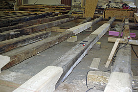 Reparaturen an den Erdgeschossdeckenbalken Fotoaufnahme der Reparaturen an den Erdgeschossdeckenbalken. Die Balken liegen sortiert in der Abbundhalle der Firma Lederer. Die Schäden an den vorderen drei Balken wurden bereits mit frischen Nadelhölzern repariert.