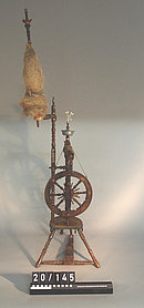 Das Spinnrad ist aus Holz. Es ist verziert. Manche Teile sind aus Zinn.