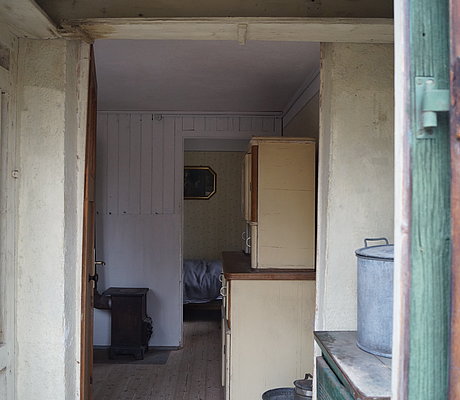 Blick in die Stube des Behelfsheimes mit Küchenschrank und Holzofen