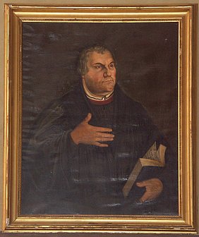 Bruststück Martin Luthers im gesetzten Alter, gekleidet mit schwarzer Schaube, in der linken Hand eine aufgeschlagene Bibel haltend, die rechte Hand erhoben